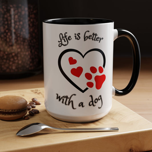 White mug with black interior and handle, featuring a heart and paw print design with text 'Life is better with a dog', on a wooden surface with coffee beans and a spoon.